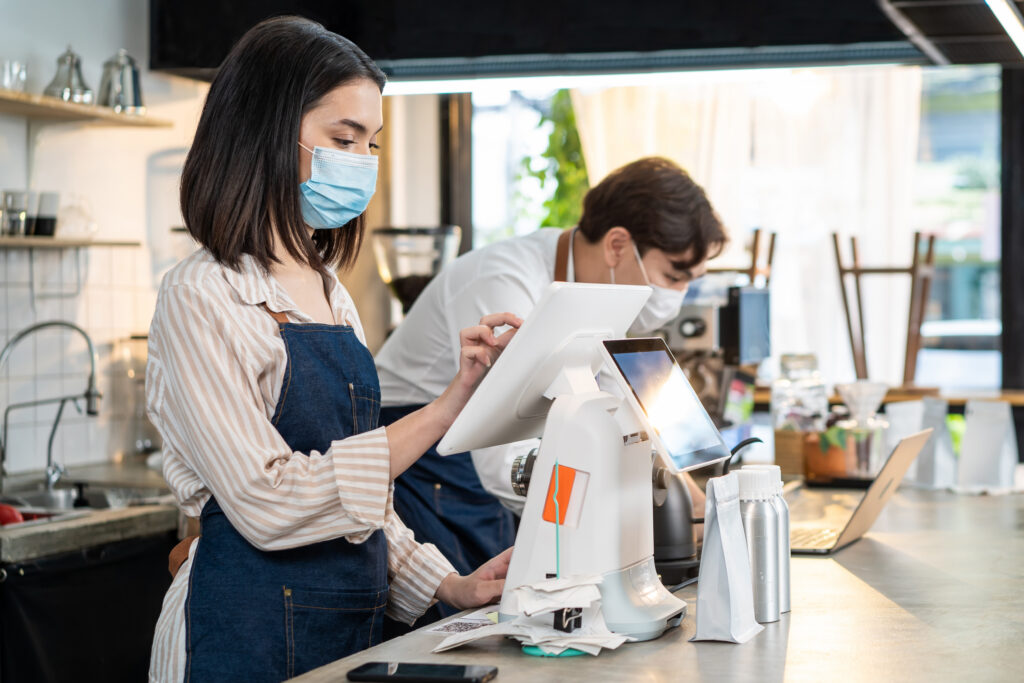 A cafe manager and employee reconciling a POS transaction against the day's bank payout at close.