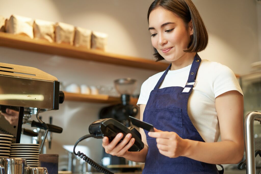 A barista taps a customer’s card at a payment terminal machine in a cafe in Malaysia.